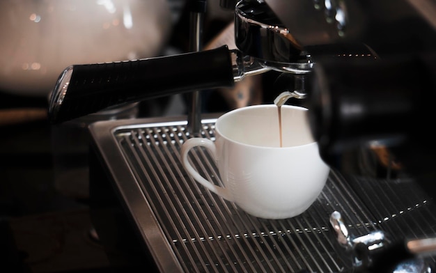 Primer plano de una cafetera vertiendo bebida en una taza en una cafetería