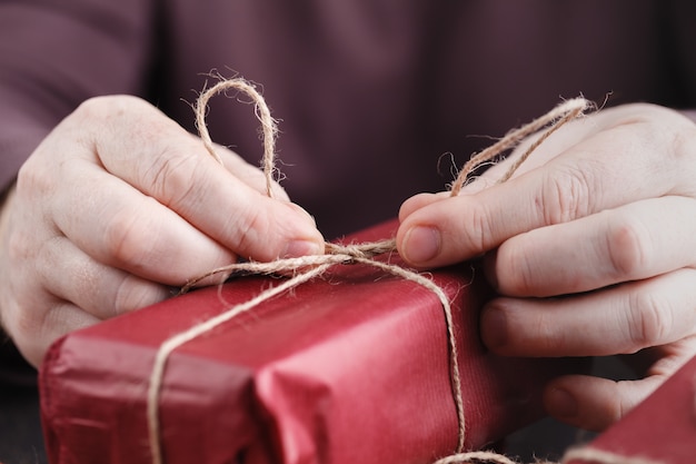 Primer plano de caja de regalo roja. Envoltura de regalos de Navidad, personas decorando regalos. Vacaciones, hecho a mano, amor, concepto sorpresa