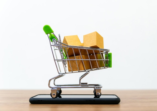 Primer plano de cajas en un pequeño carrito de compras en un teléfono inteligente en la mesa contra un fondo blanco