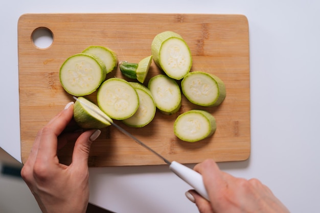 Primer plano de calabacín cortado en trozos sobre tabla de madera, vista superior, en cocina con interior moderno. Concepto de alimentación saludable.