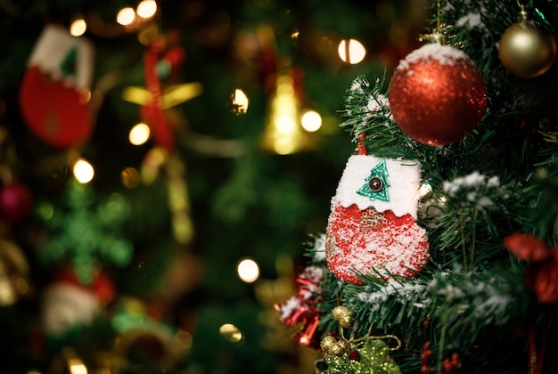 Primer plano de un calcetín decorado con nieve falsa roja y blanca que cuelga decorando en la rama de un árbol de pino de Navidad verde frente a un fondo borroso en el evento de la noche de celebración del festival tradicional de la víspera de Navidad.