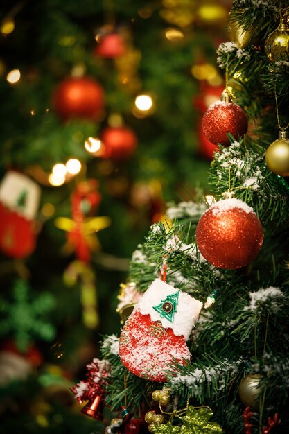 Primer plano de un calcetín decorado con nieve falsa roja y blanca que cuelga decorando en la rama de un árbol de pino de Navidad verde frente a un fondo borroso en el evento de la noche de celebración del festival tradicional de la víspera de Navidad.