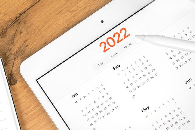 Primer plano del calendario 2022, pantalla de tableta. Fondo de escritorio de mesa de madera de negocios. Foto de concepto de planificación de citas y reuniones