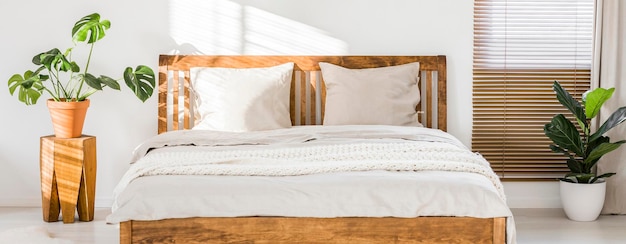 Primer plano de una cama doble de madera con ropa de cama, almohadas y manta