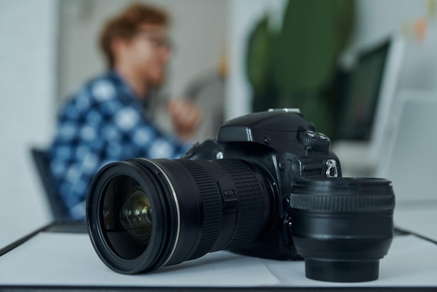 Foto primer plano de una cámara digital y un joven usando una computadora en el fondo