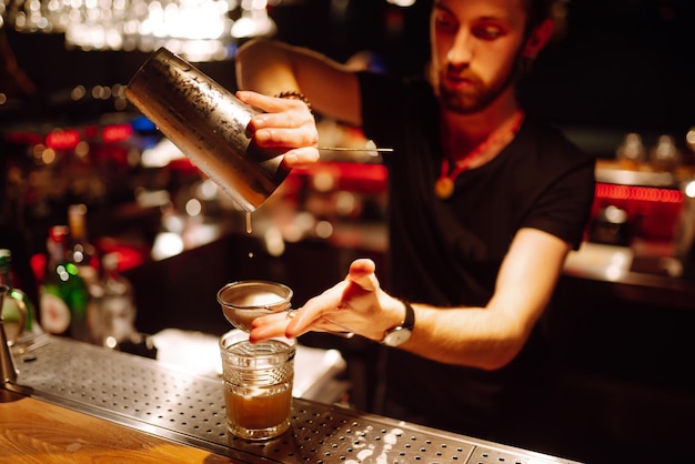 Primer plano de camarero hace un cóctel en un club nocturno Camarero profesional vertiendo de una coctelera