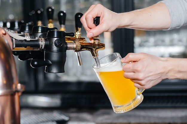 Primer plano del camarero llenando una jarra de cerveza ligera. La barra del bar en el pub.