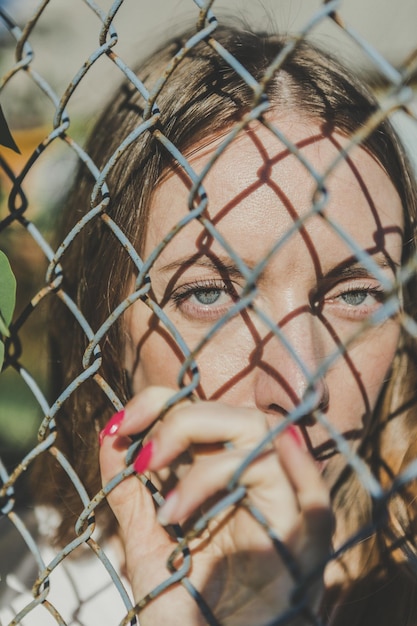 Foto primer plano de la cara de una joven detrás de una valla de metal