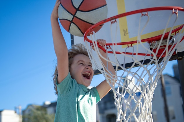 Primer plano de la cara del jugador de baloncesto infantil haciendo slam dunk durante el juego de baloncesto El jugador de deporte infantil al aire libre en el patio de juegos de baloncesto