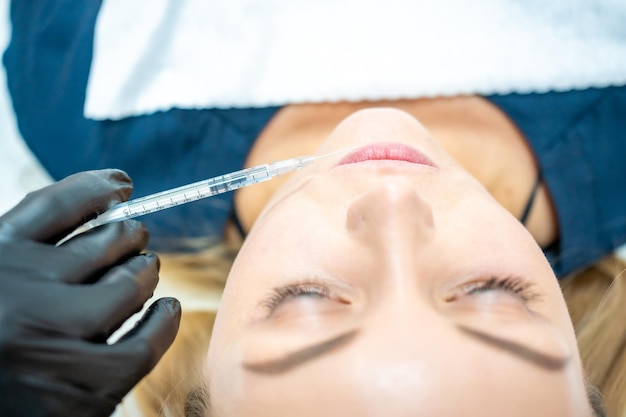 Primer plano de la cara y la mano de la mujer en guante quirúrgico sosteniendo la jeringa cerca de sus labios listos para recibir beau