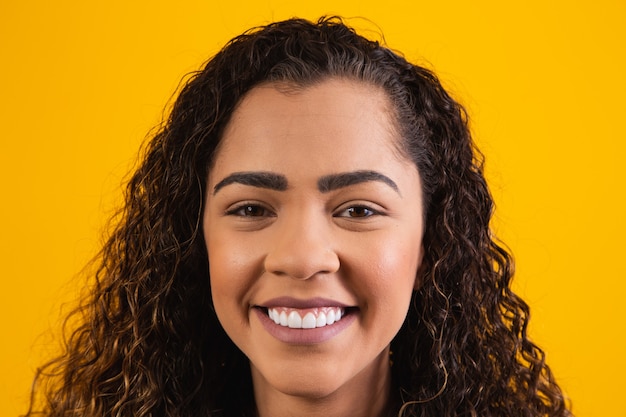 Primer plano de la cara de mujer afro sonriendo sobre fondo amarillo con espacio libre para texto. Mujer afro sonriendo.