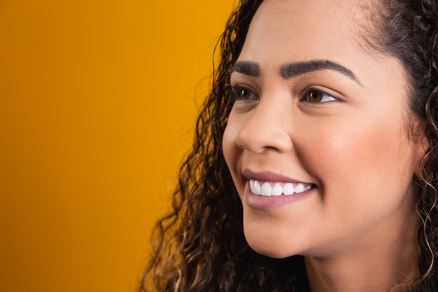 Primer plano de la cara de mujer afro sonriendo sobre fondo amarillo con espacio libre para texto. Mujer afro sonriendo.