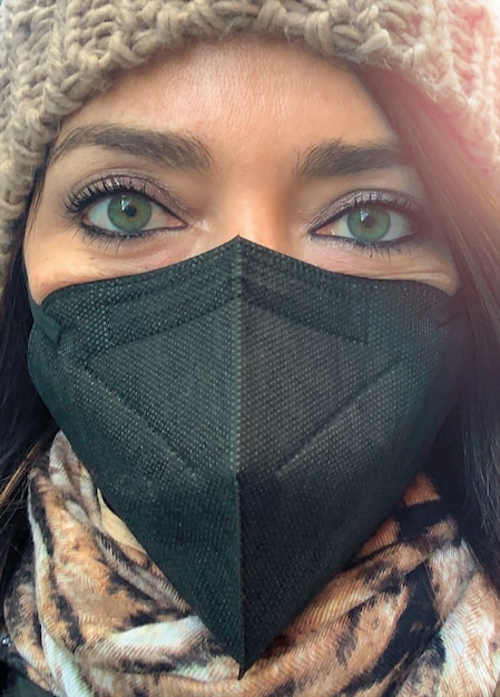 Foto primer plano de la cara de una mujer de ojos verdes vestida con traje de invierno y máscara.