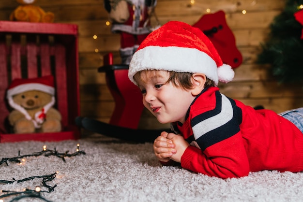 Foto primer plano de la cara de un niño alegre con una gorra roja tendido sobre un fondo de madera en navidad