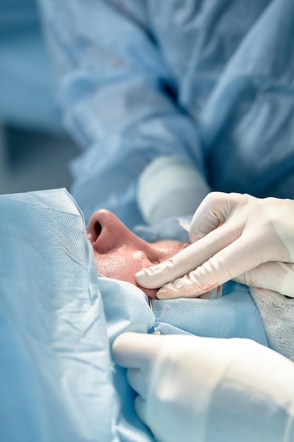 Foto primer plano de la cara de un paciente que se somete a una blefaroplastia el cirujano corta el párpado y realiza manipulaciones con instrumentos médicos