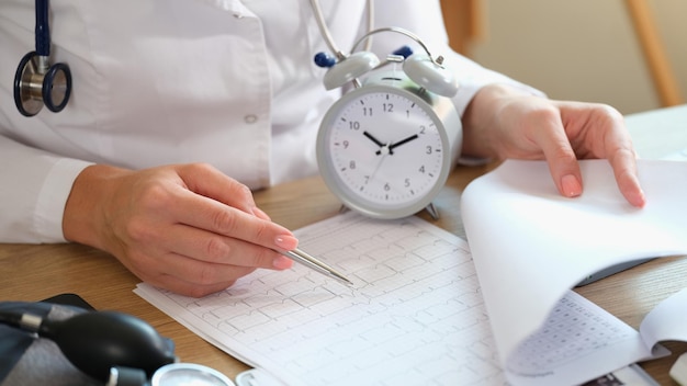 Primer plano de un cardiólogo revisando el cardiograma del paciente en el despertador de la oficina de la clínica en la mesa