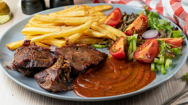 Primer plano de carne asada con salsa de verduras y papas fritas en un plato sobre la mesa