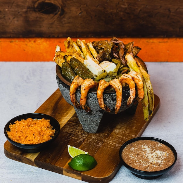 Foto primer plano de una carne mixta en molcajete junto al arroz y los frijoles en una tabla de madera