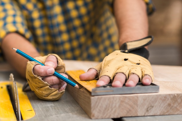 Primer plano de un carpintero que mide un bloque de madera con una regla en la mesa de trabajo