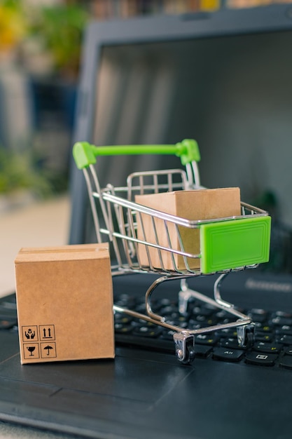 Primer plano de un carrito de compras con una caja al lado de una computadora portátil y una tarjeta de crédito en el escritorio