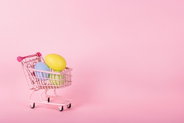 Primer plano de un carrito de compras con huevos contra un fondo rosado