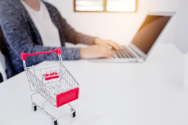 Primer plano del carrito de compras mientras el hombre usa la computadora portátil en el fondo