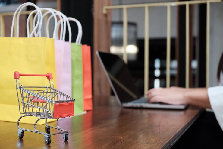 Foto primer plano de un carrito de compras en miniatura por una mujer usando una computadora portátil en la mesa