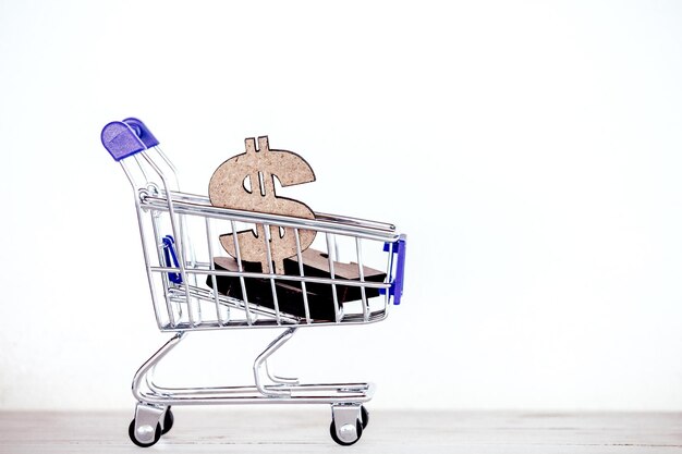 Primer plano de un carrito de compras en miniatura con el símbolo del dólar contra un fondo blanco