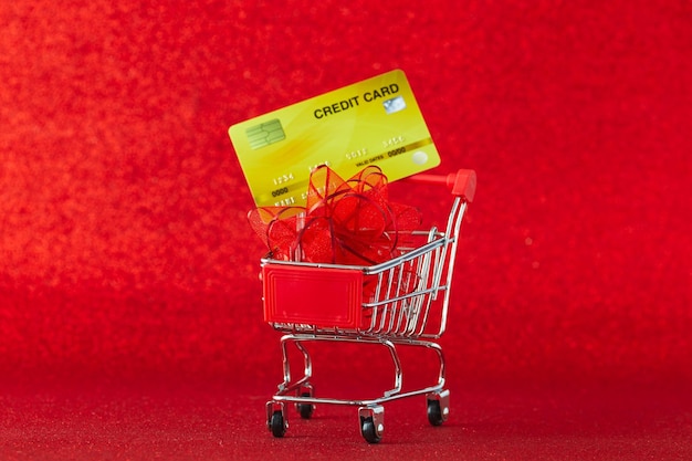 Primer plano de un carrito de compras con tarjeta de crédito contra un fondo rojo