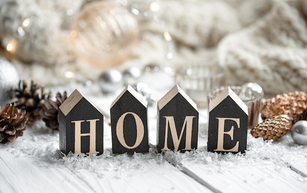 Primer plano de casa de palabra de madera decorativa sobre fondo borroso con detalles de decoración navideña.