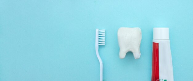 Foto primer plano de un cepillo de dientes y pasta de dientes con modelo de diente molar blanco sobre un fondo azul borroso significa cuidar la cavidad oral