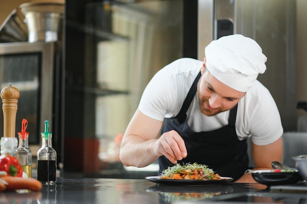Primer plano de un chef masculino concentrado guarnición de alimentos en la cocina