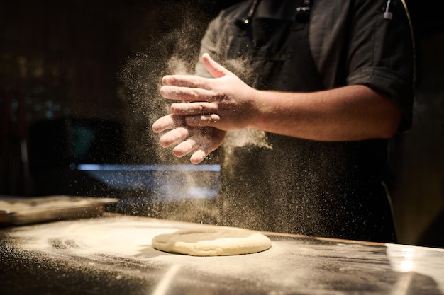 Primer plano de chef rociando harina fresca en pan plano de masa durante el trabajo