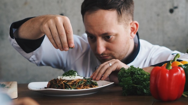 Foto primer plano del chef rociando hierbas en la comida en el plato en la mesa