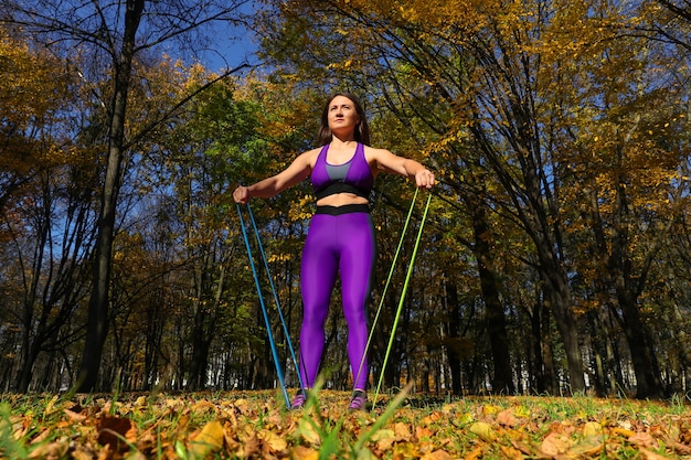 Primer plano de una chica deportiva haciendo ejercicios con una banda elástica de fitness en el parque