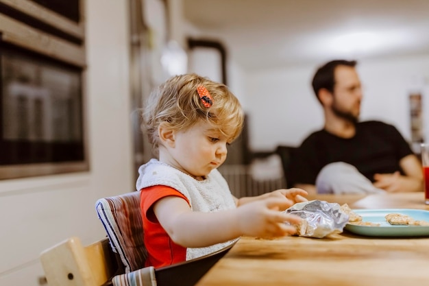 Primer plano de una chica linda comiendo galletas en la mesa en casa