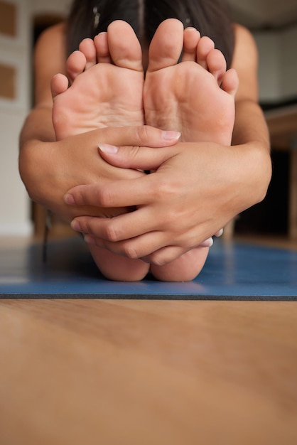 El primer plano de una chica que se estira para tocarse los dedos de los pies mientras se sienta en una alfombra de yoga