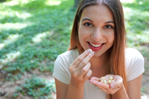 Foto primer plano de una chica sana comiendo nueces de macadamia en el parque mirando a la cámara