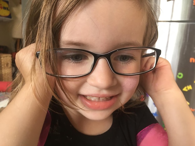 Primer plano de una chica sonriente con gafas mirando hacia casa.
