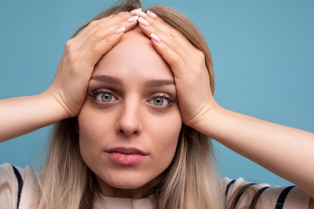 El primer plano de una chica triste con ropa informal sosteniendo su cabeza sobre un fondo azul aislado