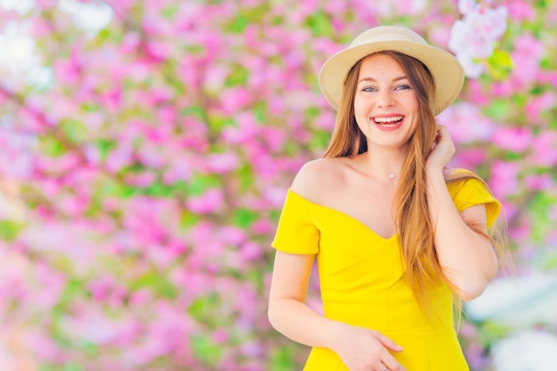 El primer plano de una chica con un vestido con los hombros desnudos y un sombrero en el fondo de un árbol con flores.