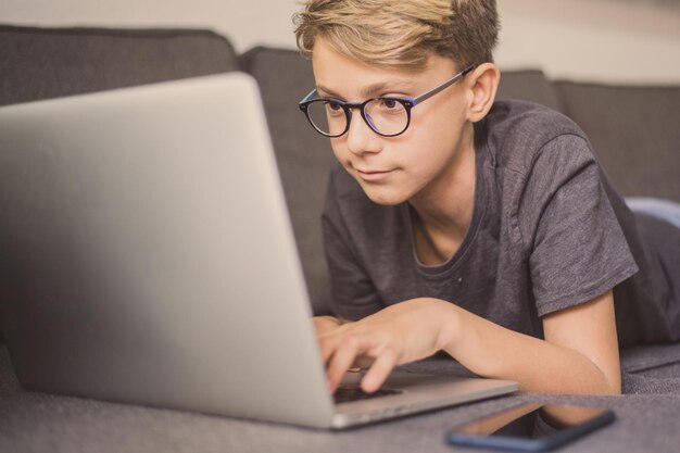 Primer plano de un chico lindo usando una computadora portátil en el sofá
