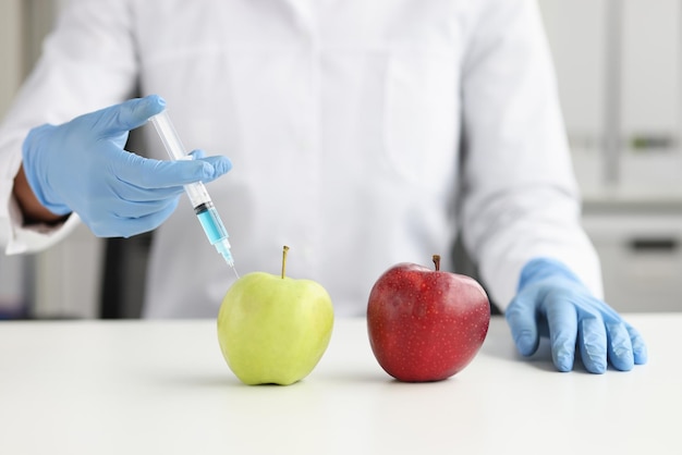 Primer plano de científico en bata blanca haciendo inyección en manzana verde en verduras de laboratorio