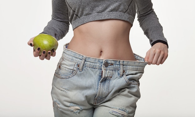 Foto primer plano de la cintura delgada de una mujer joven en jeans grandes que muestra la pérdida de peso exitosa