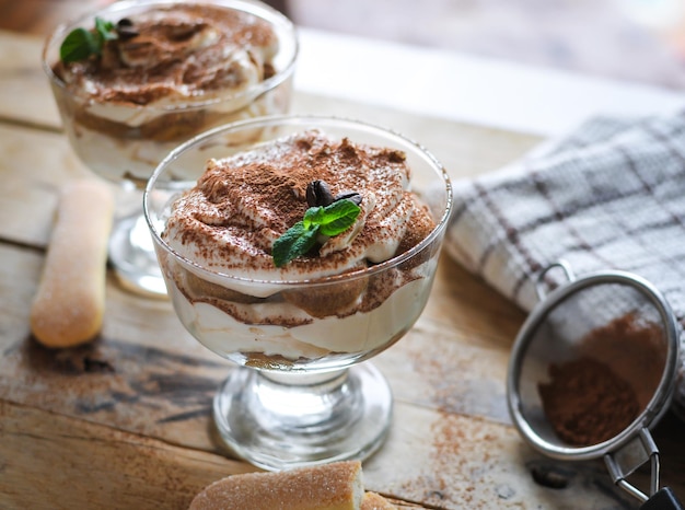 Foto primer plano de un clásico pastel de tiramisu en un vaso con menta fresca sobre un fondo de madera