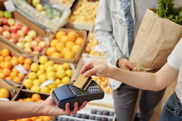 Primer plano de un cliente irreconocible que coloca la tarjeta inalámbrica en el terminal mientras usa el pago sin contacto en el mercado de agricultores