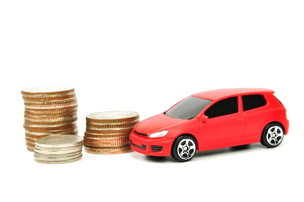 Primer plano de un coche de juguete rojo con monedas apiladas sobre un fondo blanco