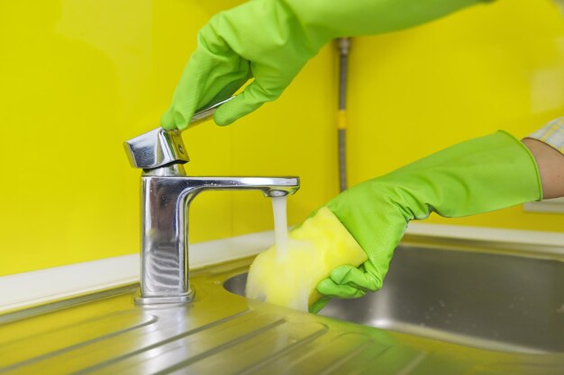 Primer plano de la cocina de limpieza, manos de mujer en guantes de goma con detergente de esponja lavando el fregadero