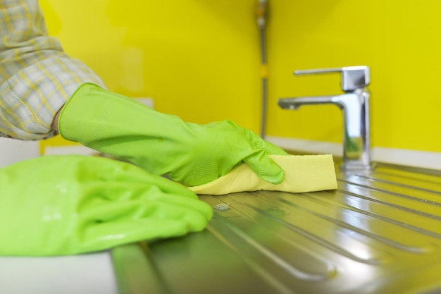 Primer plano de la cocina de limpieza, manos de mujer en guantes de goma con detergente de esponja lavando el fregadero