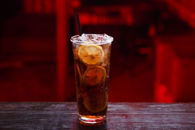 Primer plano de un cóctel Cuba Libre en vaso largo, ginebra, de pie sobre la barra del bar, aislado en un espacio de luz roja.